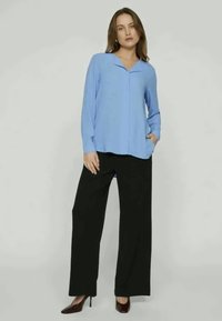 Lyseblå langermet bluse med krage, kombinert med svarte vidde bukser. Antrekket har en avslappet passform og en glatt tekstur.