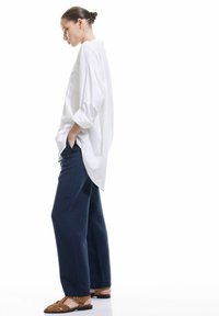 Witte oversized shirt met opgerolde mouwen, gecombineerd met marineblauwe wijde broek en bruine sandalen met bandjes. Eenvoudig, casual outfitontwerp.