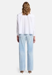 Hvid skjorte med krave og lange ærmer, cropped pasform og knapmanchetter, parret med lyseblå brede jeans med en falmet struktur.