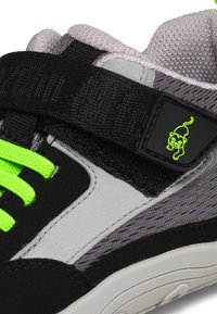 Sneaker nero e grigio con tomaia strutturata, lacci verdi e cinturino nero con logo neon a forma di scimmia. Suola in gomma con dettagli di cucitura.