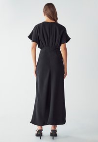Robe maxi noire avec des manches courtes évasées, taille cintrée et silhouette droite, dotée d'une fermeture éclair dissimulée au dos et d'une texture lisse.