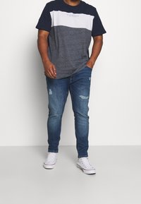 T-shirt color bloc en bleu marine et gris avec un col rond, associé à un jean déchiré bleu clair et des baskets blanches.