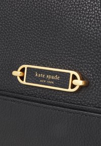 Black textured leather bag featuring a gold-tone plaque with "kate spade NEW YORK" embossed. Structured design with a smooth finish.