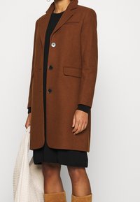 Brun uldblandingsfrakke med skræddersyet design, reverskrave, tre knapper, sidelommer og kontrasterende sorte manchetter.