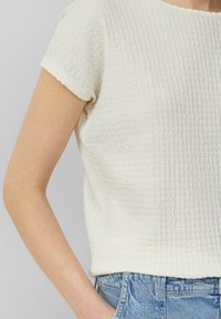 Vit texturerad kortärmad topp med en fyrkantig snitt, försedda med ett subtilt rynk-mönster, matchad med ljusblå denimshorts.