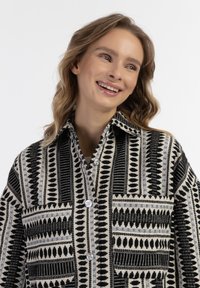 Juodas ir kreminės spalvos raštuotas švarkas su kontrastingomis tekstūromis, su mygtukų užsegimu, dviem krūtinės kišenėmis ir apykaklės dizainu.