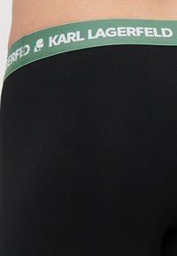Črne spodnjice z zelenim elastičnim pasom, na katerem je besedilo in logotip "KARL LAGERFELD". Gladek material z oprijetim fit.