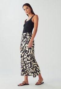 Czarny top na ramiączkach połączony z długą, zwiewną spódnicą z odważnym czarno-kremowym, abstrakcyjnym wzorem. Całość uzupełniają płaskie czarne sandały.