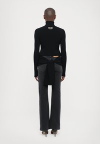 Svart ribbestrikket turtleneck genser med en cropped design, med et knyttet tillegg bak, sammen med høy midje grå flagrende jeans.