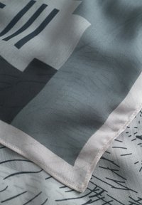 Foulard en soie avec des motifs géométriques dans des tons atténués de gris, offrant une texture lisse et un ourlet cousu soigné le long du bord.