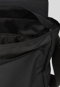 Sac messager noir avec une fermeture éclair extérieure lisse, une bandoulière réglable et un intérieur spacieux avec des poches en maille.