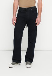 Granatowe spodnie z denimu o luźnym kroju, z regulowanym pasem, przednimi kieszeniami i subtelnymi detalami przeszyć. Stylizowane ze szarymi trampkami.