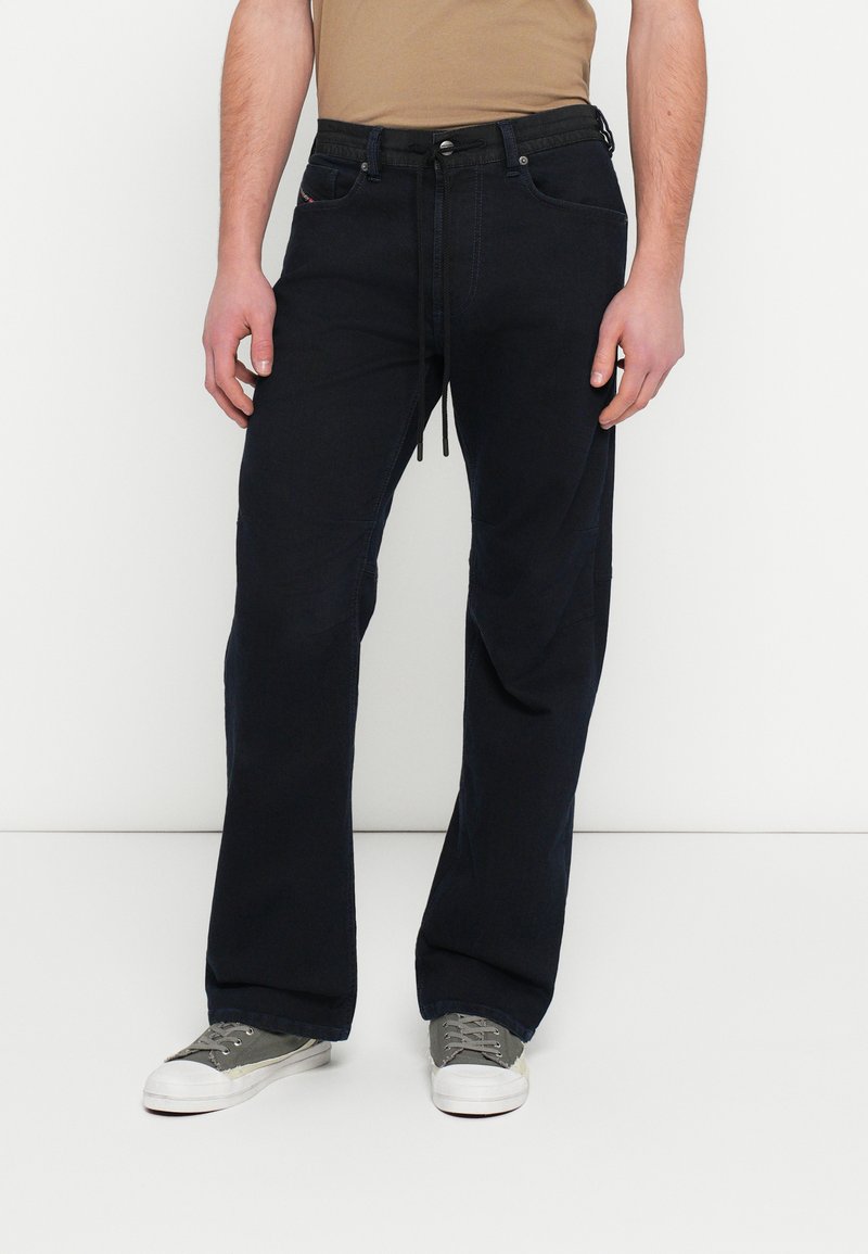 Granatowe spodnie z denimu o luźnym kroju, z regulowanym pasem, przednimi kieszeniami i subtelnymi detalami przeszyć. Stylizowane ze szarymi trampkami.