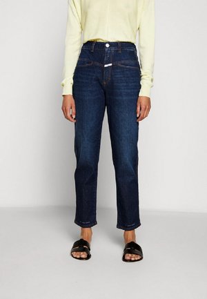 Dark blue high-waisted jeans with a straight leg, featuring five pockets, a zip fly, and a button closure. Paired with a light yellow top and black sandals.
