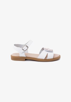 White sandal made of synthetic material, featuring a simple design with an adjustable ankle strap, floral accent, and a tan outsole.