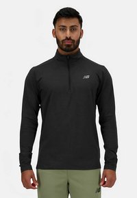 Musta pitkähiha-vetoketjullinen paita, valmistettu pehmeästä materiaalista, jossa korkea kaulus ja pieni heijastava logo rinnassa.