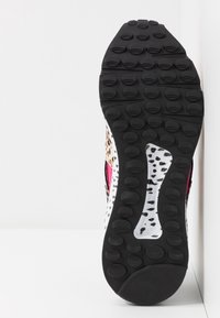 Semelle en caoutchouc d'une chaussure de sport avec des motifs circulaires et un imprimé animalier en noir, blanc, rose et beige.