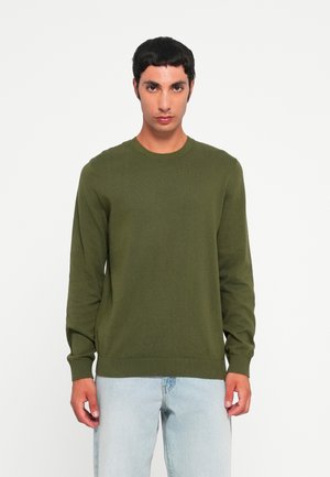 Groene gebreide trui met een ronde hals en lange mouwen, voorzien van ribgebreide boorden en onderrand, gecombineerd met lichtblauwe jeans.