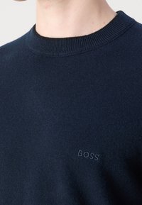 Námořnický modrý svetr s žebrovaným kulatým výstřihem. Obsahuje jemné logo "BOSS" vyšitěné v přiřazené barvě. Měkká, hladká textura.