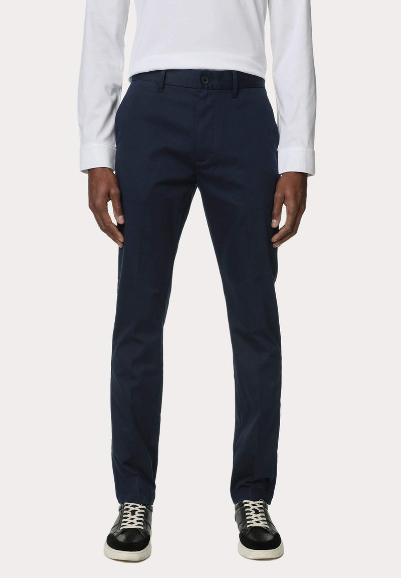 Pantalones de vestir azul marino de corte recto, con trabillas para cinturón y bolsillos laterales, combinados con zapatillas negras y una camisa de manga larga blanca.