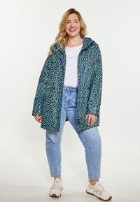 Blå leopardmönstrad regnjacka med huva, tillverkad av ett glänsande material; ihop med ljusblå jeans och vita sneakers.