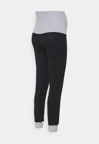 Zwangere leggings met een hoge, gestreepte tailleband. Zwarte stof met witte stippen, taps toelopende pasvorm met gestreepte omslagen.