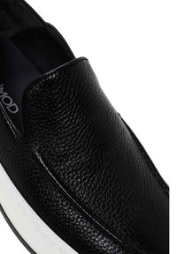 Black leather slip-on shoe with a textured surface, rounded toe, and elastic gussets, featuring a white rubber sole and minimal branding.