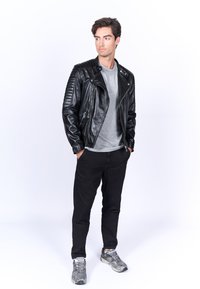 Giacca da motociclista nera in pelle con texture a coste sulle spalle, indossata sopra una t-shirt grigia, abbinata a pantaloni neri e sneakers grigie.