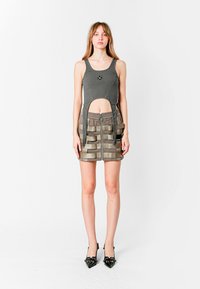 Top gris sin mangas con un corte circular y logo. Falda mini gris a juego con tiras en capas y detalle de cremallera lateral.