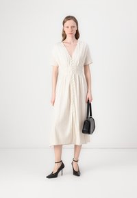 Abito midi color crema con maniche corte, scollatura a V, righe verticali, chiusura con bottoni e vita smock. Abbinato a tacchi neri e borsa.