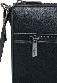 Crna teksturirana kožna torba pravokutnog oblika, s patentnim zatvaračem na vrhu, srebrnim dodacima i malim detaljem u obliku patentnog zatvarača.