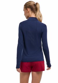 Granatowa, długorękawowa sportowa koszulka z teksturowanej tkaniny, z siateczkową wkładką na plecach i dopasowanym krojem, zestawiona z czerwonymi szortami.