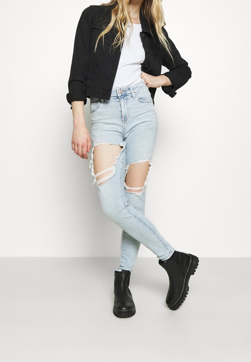 Mörk denimjacka, vit t-shirt, ljusblå ripped skinny jeans med stora öppningar, svarta ankelskor med tjocka sulor.