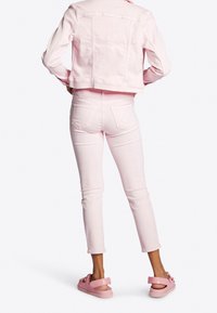 Chaqueta de mezclilla rosa pálido y jeans ajustados con un diseño recortado; combinados con sandalias rosa claro que presentan lazos en las correas.