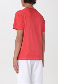 T-shirt rossa in cotone con collo rotondo e maniche corte, dal taglio rilassato e texture morbida. La vista posteriore mostra dettagli di design minimi.