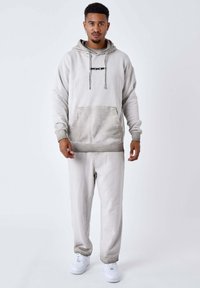 Felpa grigia chiara con tasca frontale, coulisse e logo. Abbinata a pantaloni jogger coordinati e sneakers bianche. Materiale misto cotone.