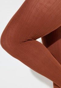 Leggings marrones con textura que presentan un patrón geométrico, un diseño curvado y un material suave con detalles acanalados a lo largo de las costuras.