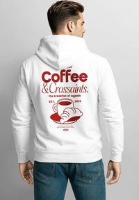 White hoodie featuring red text that reads "Coffee & Croissants." with graphic of a cup and croissant. Simple design and soft fabric.