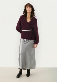 Maglione avvolgente borgogna in pelliccia, gonna massima in satin argento, semplici ballerine nere. Il maglione ha maniche larghe, cintura argentata decorata e una consistenza liscia.