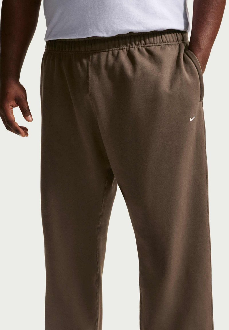 Pantaloni della tuta Nike in verde oliva, con vita elasticizzata, tasche laterali e un piccolo logo bianco sulla coscia sinistra. Tessuto dalla trama morbida.