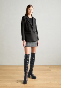 Black blazer with single button, two front pockets, paired with a patterned mini skirt. Black knee-high heeled boots add contrast.