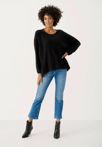 Schwarzer, locker sitzender Pullover mit rundem Ausschnitt, kombiniert mit hellblauen, knöchellangen Jeans und schwarzen Stiefeletten. Glatte Textur, lässiges Design.
