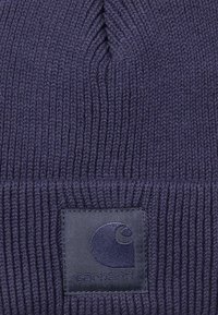 Beanie in maglia navy realizzato in tessuto a coste, con una toppa quadrata con un'onda stilizzata. La texture è morbida ed elastica.