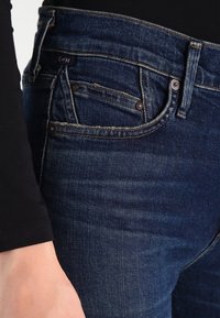 Mörkblå denimjeans med smal passform, femficksdesign, metallbeslag och synliga sömnadsdetaljer.