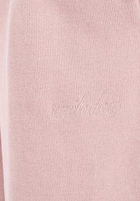 Zbliżenie na jasnoróżową prążkowaną tkaninę z delikatnym haftem w kolorze nici, przedstawiającym kursywny napis "mahlodero".