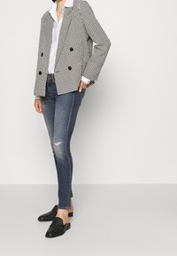 Blazer a rayas blanco y negro de doble botonadura con botones negros, combinado con jeans ajustados destrozados de color azul oscuro y mocasines negros.