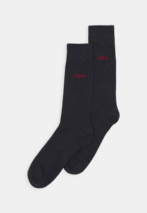 Calze grigio scuro realizzate in un materiale morbido. Caratterizzate da un polsino a coste e dal logo rosso "HUGO" sul lato, con una struttura complessivamente liscia.