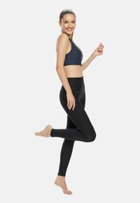 Leggings nere e un reggiseno sportivo blu navy. I leggings hanno una texture liscia, mentre il reggiseno presenta un design semplice. La modella posa di lato.