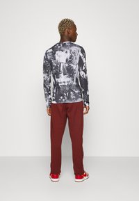 Černobílá košile s dlouhými rukávy a grafickými potisky, kombinovaná s vínovými tepláky. Obuv má červený design s bílou podrážkou.