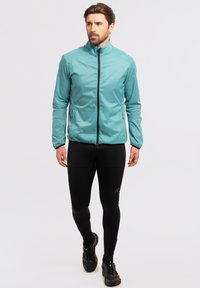 Lichtgewicht aqua jack met een opstaande kraag, een volledige rits en lange mouwen. Gecombineerd met zwarte sportleggingen en zwarte sneakers.